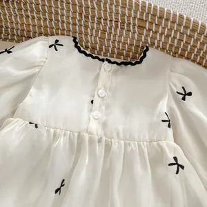 Detail of baby romper featuring black wave trim collar and bow embroidery on cream fabric