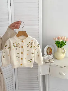 Detail van crème gebreid vest met bloemenborduurwerk en getextureerde gele knopen