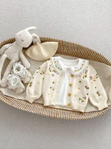 Detail van bloemenborduurwerk op gebreid babyvestje en vintage geweven wiegenset