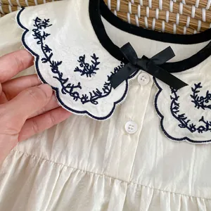 Beige babyrompertje met geborduurde golfkraag en een zwart strikje als detail