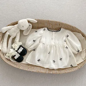 Flat lay of baby girl mesh romper with black bow embroidery in a woven cradle