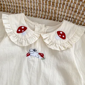 Dettaglio del colletto ricamato con funghi e motivo a coniglio su camicia in cotone crema