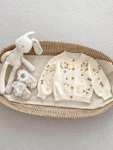 Detail van bloemenborduurwerk en houten knopen op een gebreid babyvest van katoen