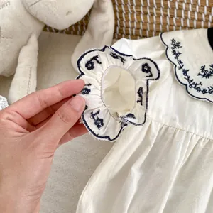 Detailopname van witte babyromper met bloemenborduursels en ruches aan de mouwen