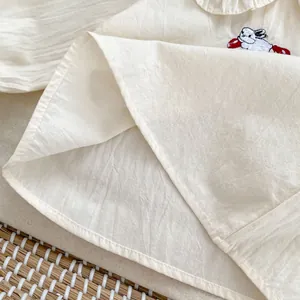 Dettaglio del ricamo a coniglio su camicia in cotone crema con cuciture rifinite