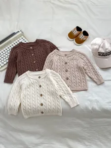 Detail of cable-knit baby sweaters with wooden buttons in various neutral colors
