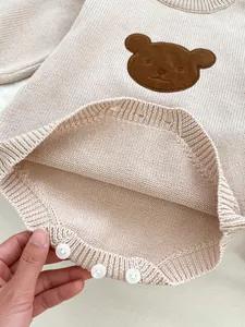 Détail d'un body en tricot pour bébé avec écusson ours brun et boutons à l'entrejambe