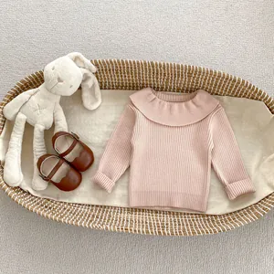 Detailed knit texture of pink ruffled collar sweater with baby shoes and plush rabbit