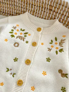 Detailopname van katoenen babyvestje met bloemenborduurwerk en barnsteen knopen