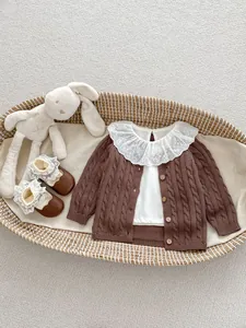 Detail of baby knit cardigan with lace collar and matching brown leather shoes in a basket