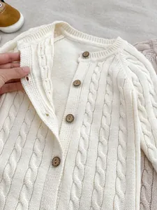 Dettaglio tutina neonato a maglia a trecce con bottoni in legno e morbido cotone crema