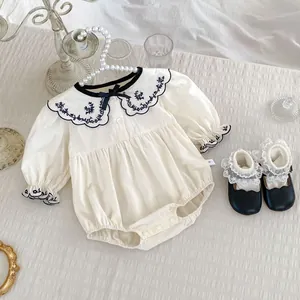 Detail van babyrompertje met marineblauw geborduurde kraag en kanten schoenenset
