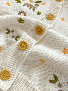 Detailopname van katoenen gebreid vest met bloemmotieven en amberkleurige knopen