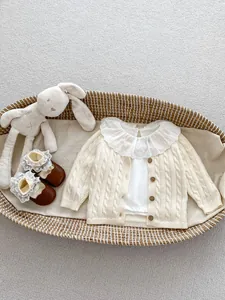 Detail of beige cable knit infant cardigan with wooden buttons and lace collar insert