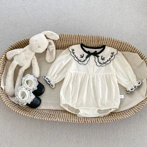 Detail van babyromper met geborduurde schulprandkraag en strik in een geweven mand
