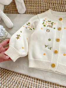 Detail van bloemenborduurwerk en houten knopen op een gebreid katoenen babyvestje