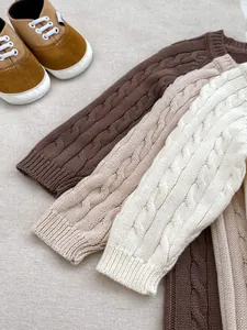 Dettaglio dei polsini in maglia a trecce su pagliaccetti neonato marrone, albicocca e panna