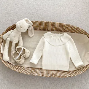 Détail d'un pull en tricot blanc pour bébé avec col à volants et chaussures à nœud décoratif
