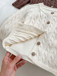 Detailed view of cable-knit texture and wooden buttons on a beige cotton baby cardigan