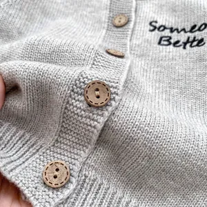 Dettaglio del cardigan grigio in maglia con bottoni in legno e ricamo 'Someone Better'