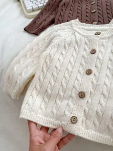 Detail of cable-knit textures and round wooden buttons on baby cardigans in cream and coffee