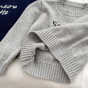 Close-up of a light grey round neck knit sweater featuring ribbed cuffs and hem details