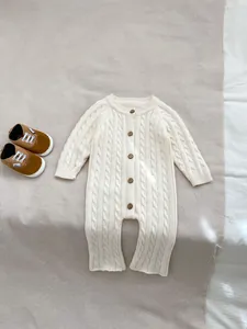 Dettaglio della tutina in maglia a trecce color crema con bottoni in legno naturale