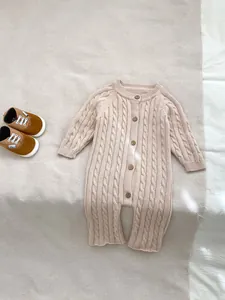 Dettaglio di pagliaccetto per neonato in maglia beige con motivi a treccia e bottoni