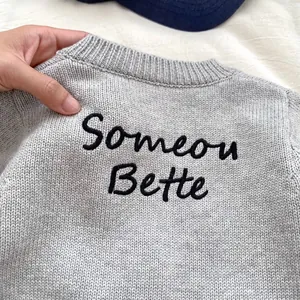 Dettaglio del cardigan grigio in maglia con ricamo Someone Better e colletto a costine