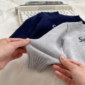 Close-up of crewneck knit sweaters featuring letter embroidery and ribbed cuffs
