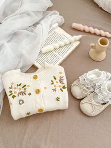 Detailopname van bloemenborduurwerk op gebreid babyvest met houten knopen en kant