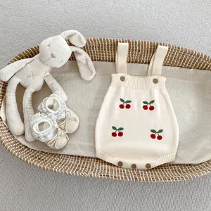Dettaglio tutina in maglia per neonato con ricamo ciliegia e bottoni in legno nel cesto