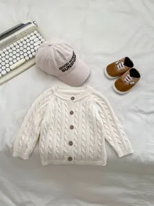 Detailed close-up of cream cable knit cardigan with vintage wooden buttons and matching cap