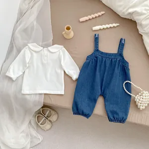 Detail of baby denim overalls with white embroidered straps and Peter Pan collar shirt