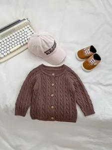 Close-up of brown cable knit baby cardigan with vintage wooden buttons and cotton cap