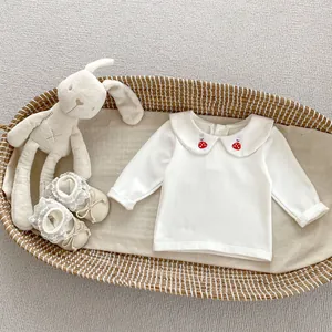 Close-up of white cotton baby top with rabbit embroidery on Peter Pan collar