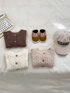 Flat lay of baby knit sweaters, sneakers, and embroidered hat on white fabric
