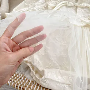 Macro shot of delicate embroidered lace and soft mesh layer on a cream infant bodysuit