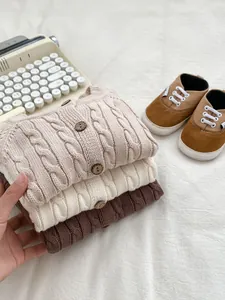 Close-up of three knitted baby cardigans with cable patterns and wooden buttons