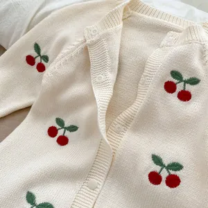 Dettaglio del cardigan in maglia per neonati con ricamo di ciliegie e bottoni bianchi