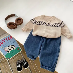 Detailed flat lay of boys beige knit sweater with wave patterns and blue denim jeans