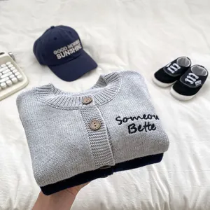 Dettaglio del cardigan in maglia grigia per neonato con ricamo e bottoni decorativi
