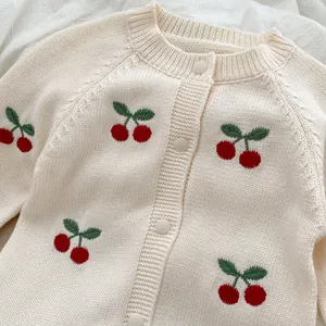 Dettaglio del cardigan in maglia crema per neonati con ricamo ciliegia rossa e bottoni