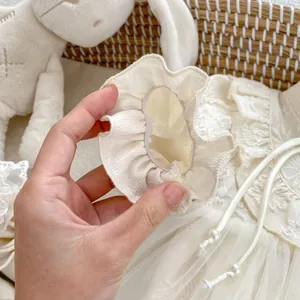 Close-up of baby romper with floral embroidery lace sleeves and pearl drawstring detail