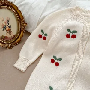 Dettaglio del cardigan in maglia color crema per neonati con ricami a ciliegia e bottoni