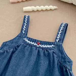 Detail of baby denim dress with mushroom embroidery and white leaf stitching on straps