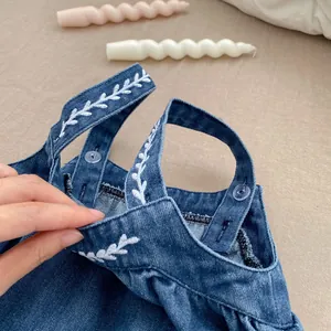 Detail of dark blue denim overalls featuring white leaf embroidery and transparent buttons