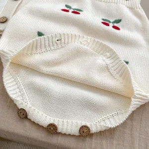 Dettaglio tutina neonato in maglia con ricamo a ciliegia e bottoni in legno naturale