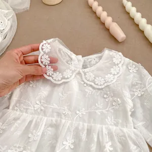 Detail of white baby romper featuring intricate daisy embroidery and Peter Pan collar