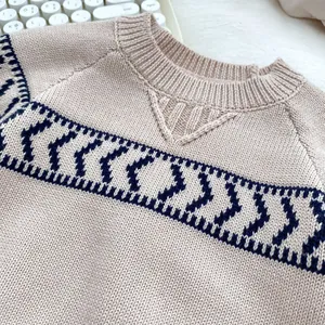 Detail of beige knit sweater showing ribbed crew neck and navy geometric pattern